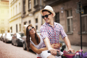 young smiling man riding a bike with a beautiful woman behind him